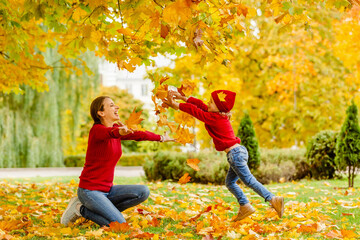 a girls in a red knitted clothes throws up yellow maple leaves in an autumn park