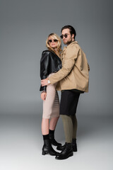 Wall Mural - full length of stylish man in autumnal outfit and sunglasses posing with woman on grey