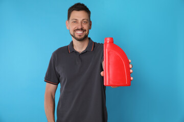 Wall Mural - Man showing motor oil against light blue background, focus on container