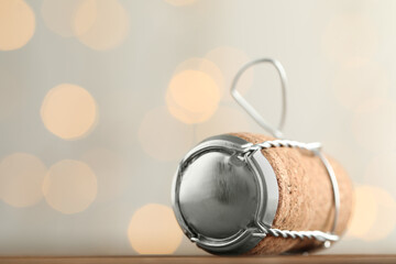 Sparkling wine cork with muselet cap on table against blurred festive lights, closeup. Space for text