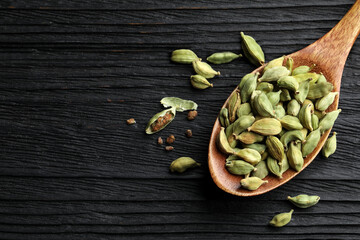 Wall Mural - Spoon with dry cardamom pods on black wooden table, top view. Space for text