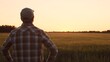 © Acronym - Farmer in front of a sunset agricultural landscape. Man in a countryside field. Country life, food production, farming and country lifestyle concept.