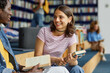 © Seventyfour - Vibrant shot of two young students chatting in college library and holding books