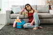 depressed asian wife sitting on  floor with a bucket of cleaning tools and propping her head on sofa is lacking desire to do house chores during daytime at home