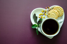 Flatlay A Cup Of Coffee And Two Small Round Delicious Cookies On A Saucer In The Shape Of A Heart Lies A Twig With Small Yellow Flowers And Leaves In The Lower Corner, Flat Lay White On A Dark Purple 