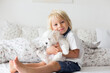 Cute little blond child, toddler boy, reading book with white puppy maltese dog