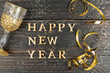 Leinwandbild Motiv Happy new year greeting card. Glass of champagne and serpantine of gold color on wooden table with scattered confetti.