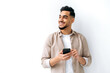 © Kateryna - Confident positive handsome indian or arabian young man, holding smartphone in hand, chatting online, browsing internet, looking happily to the side, standing on isolated white background, smiling