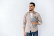 © Kateryna - Positive friendly modern arabian or indian young man with beard, wearing casual shirt, standing on isolated white background, holding laptop, looking to the side, smiling, dreaming, thinking