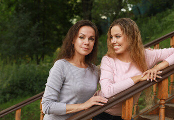 Beautiful mother and adult daughter, two generations. Summer day in the park.