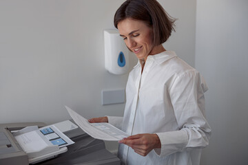 Smiling woman worker scanning a document on photocopy machine In modern office. Blurred background