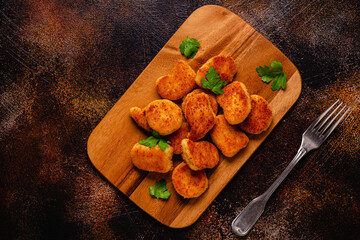 Wall Mural - Fried crispy chicken nuggets on a wooden serving board.