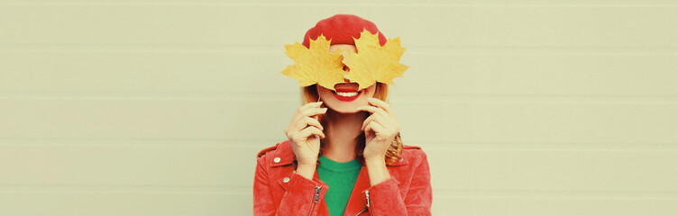 autumn portrait close up of happy woman covering her eyes with yellow maple leaves on gray backgroun