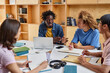 © Seventyfour - Diverse group of young students working on project together while sitting at table in library lounge