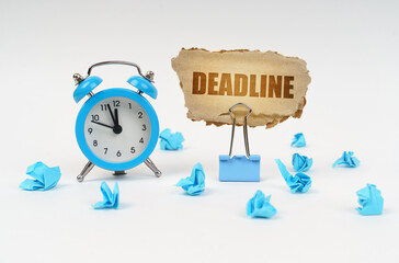 Wall Mural - On a white surface, an alarm clock, an office clip, crumpled paper and a cardboard sign with the text - Deadline