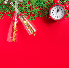 Wall Mural - Alarm clock  with tree branches and glasses of champagne on red paper background. 5 minutes before the New Year. Creative greeting card.