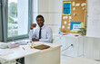 © Seventyfour - Portrait of young black teacher smiling at camera while sitting at desk in empty classroom, copy space