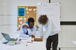© Seventyfour - Portrait of young black teacher helping boy with task or grading homework in school classroom