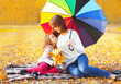 Happy mother and child little girl with umbrella and yellow maple leaves in sunny autumn park