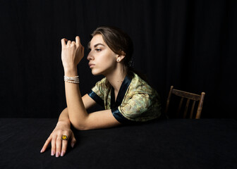 portrait of a beautiful woman with pearl jewelry and a bright ring on a black background sitting at a table