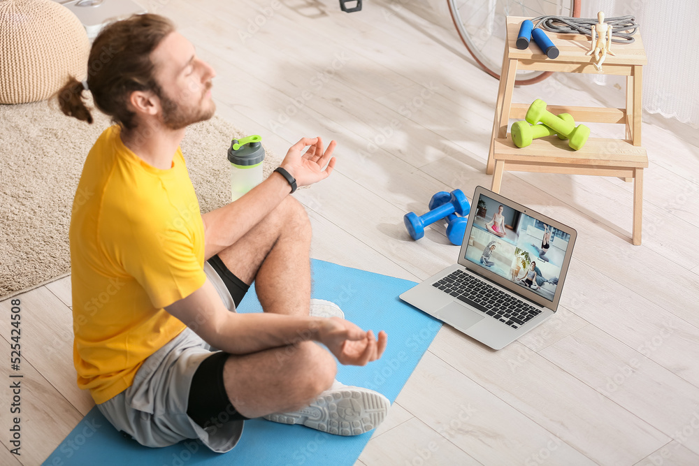 Young man using laptop for practicing yoga online at home