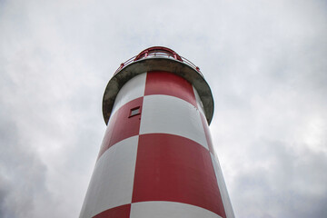 Exterior of a red and white steel and concrete lighthouse set against dramatic sky, nobody