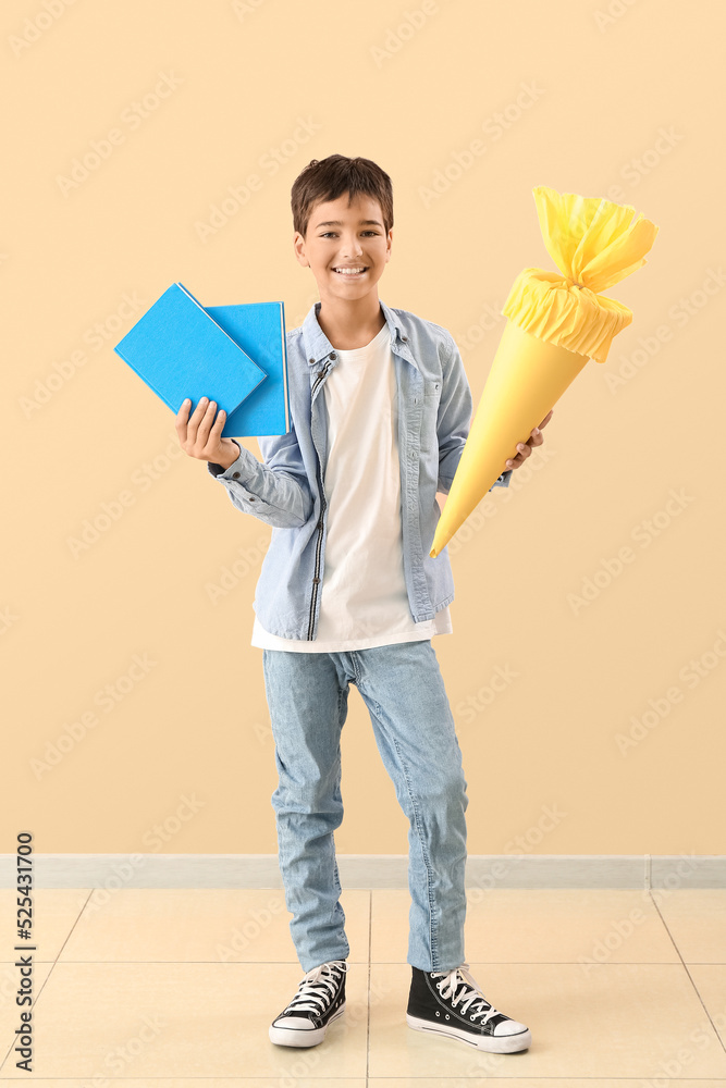 Little boy with yellow school cone and books on beige background