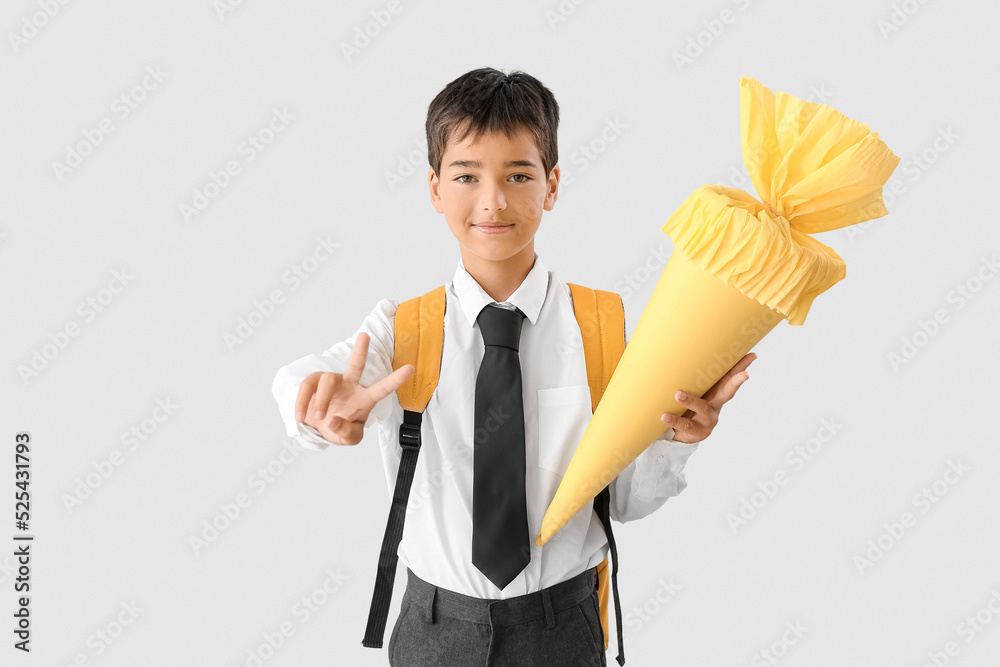 Little boy with yellow school cone showing victory gesture on light background
