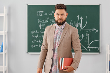 Canvas Print - Handsome Math teacher with books in classroom