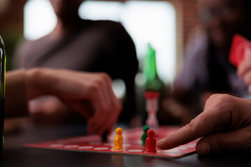 Wall Mural - Close up of people hands moving plastic figurines on game table while sitting at table. Group of friends playing boardgames together while enjoying snacks and cold beverages.