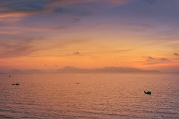 Wall Mural - Beautiful cloudscape over the sea, sunrise shot. Lonely boats. Vung Tau beach, Vietnam with beautiful yellow sunrise sky, sun and clouds in orange and blue tones.