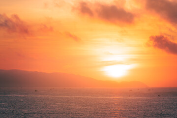 Wall Mural - Beautiful cloudscape over the sea, sunrise shot. Lonely boats. Vung Tau beach, Vietnam with beautiful yellow sunrise sky, sun and clouds in orange and blue tones.