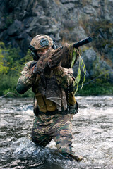 Wall Mural - Close-up photo of a mercenary military sniper during a sabotage mission behind enemy lines - he stands knee-deep in the river and aims at the enemy.