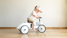 Toddler Driving Beige Retro Car. Happy Small Boy Sitting On Vintage Toy Car. Kid Playing In Nursery Room. Happy Child Riding Toy Vintage Car. Funny Kid Playing At Home