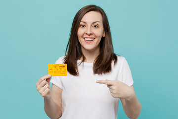 Wall Mural - Young fun surprised happy caucasian woman 20s she wear white t-shirt hold in hand point index finger on mock up of credit bank card isolated on plain pastel light blue cyan background studio portrait.