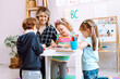 © Татьяна Волкова - Portrait of young woman sitting at table around children playing. Teacher watching pupils completing tasks in classroom.