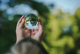 Fototapeta Pokój dzieciecy - hands holding transparent glass ball or  crystal who reflects trees of a forest outside in green nature sphere symbolizing save the earth or planet