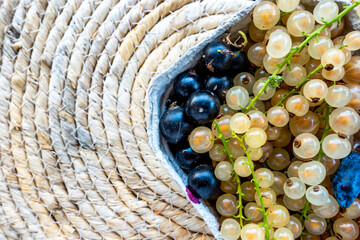 Wall Mural - A composition of red, black and white currants in a basket on the background of a mat on the table. Natural, soft light