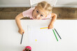 The child girl draws with colored pencils sitting at a white table. Top view, flat lay