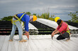 © เลิศลักษณ์ ทิพชัย - Two construction workers installing a new roof wear safety vests and safety harnesses to work on the steel roof structure.