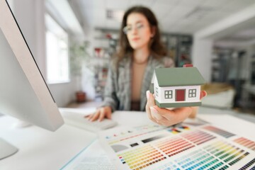 Sticker - Young beautiful woman in suit holding small model house over background studio