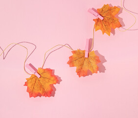 Autumn creative layout made with leaves on the rope with pink clothes hanging clips on pastel pink background. Vintage retro aesthetic 80s or 90s fashion concept. Minimal autumn season idea.