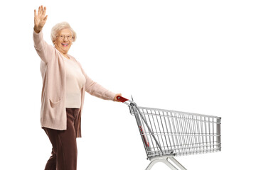 Wall Mural - Elderly woman waving and pushing an empty shopping cart