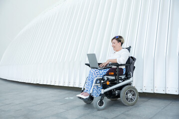 smiling woman in wheelchair uses laptop outdoors for remote work, providing job opportunities for people with disability