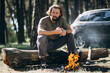 © Petro - Handsome man sitting on the log by the fire in forest drinking hot tee from thermos