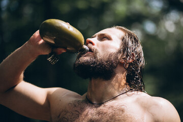 Wall Mural - Naked man drinking man from bottle in forest