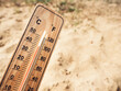 Wooden thermometer showing high temperatures over 36 degrees Celsius on sunny day on background of dry sandy ground. Concept of heat wave, warm weather, global warming, climate change.