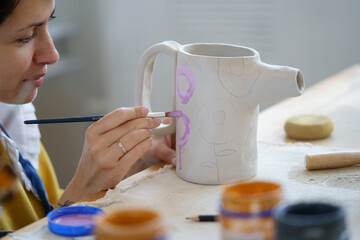 Artist woman with paintbrush create ornament on clay jug in pottery studio. Young craftswoman ceramics workshop owner, student on art classes work with potter. Ceramist professional workplace concept