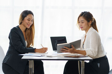 Wall Mural - Two Asian business women talk, consult, plan work on the presentation of a new start-up project idea analysis of marketing plans and investments in the office.