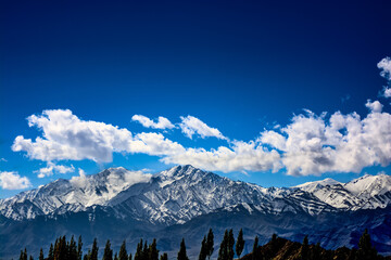 Snow covered mountains against deep blue sky and white clouds